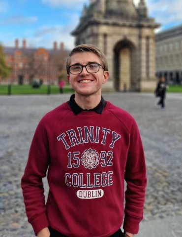 Student wearing a burgundy sweater standing in Front Square at Trinity College Dublin