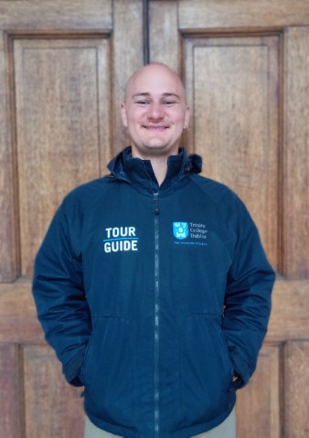 Tour guide smiling on front of a wooden door in Trinity