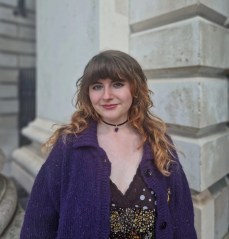 A student stands in Trinity's Front Square in a purple cardigan