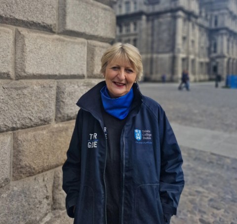 A female tour guide in a navy jacket and blue scarf standing in the Front Square at Trinity