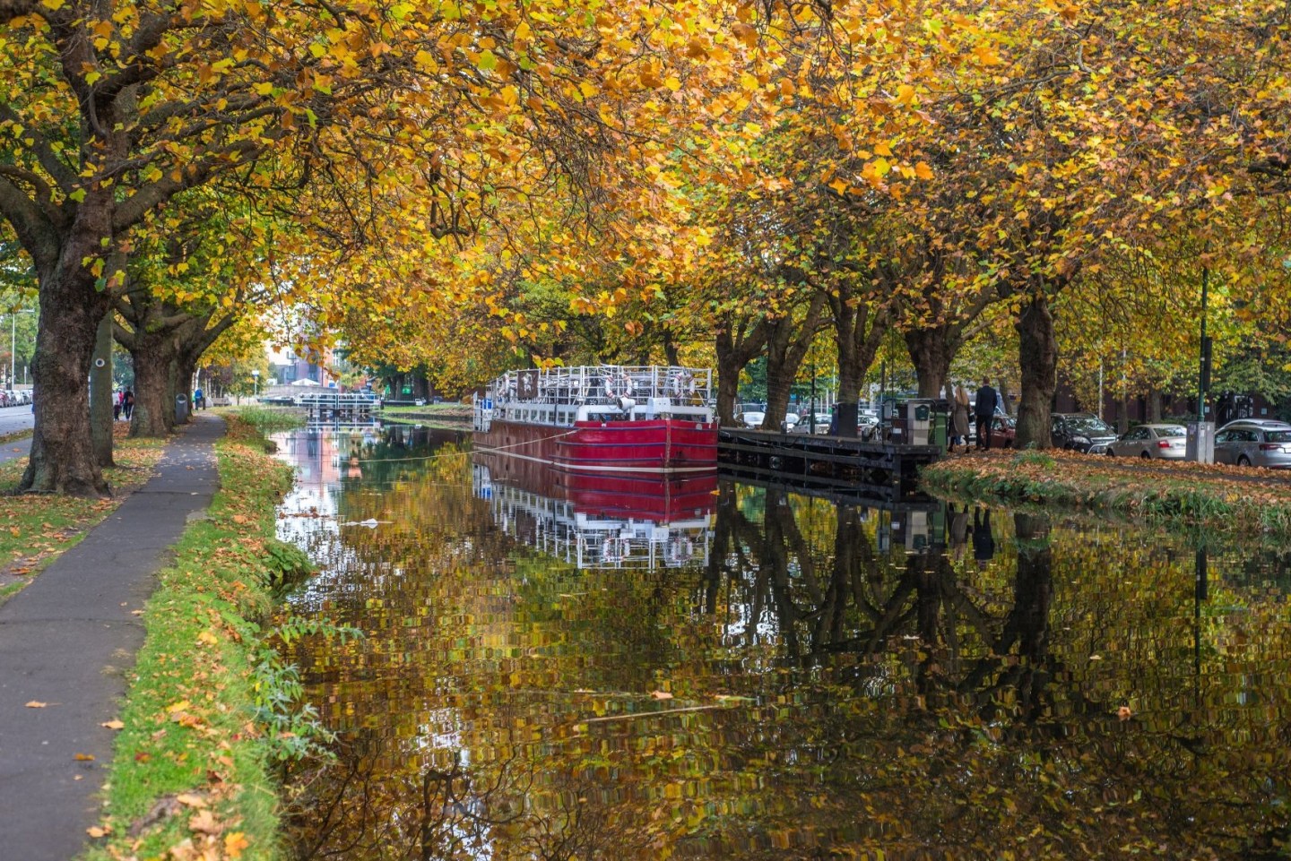 Autumn leaves reflect on a river with a red canal boat