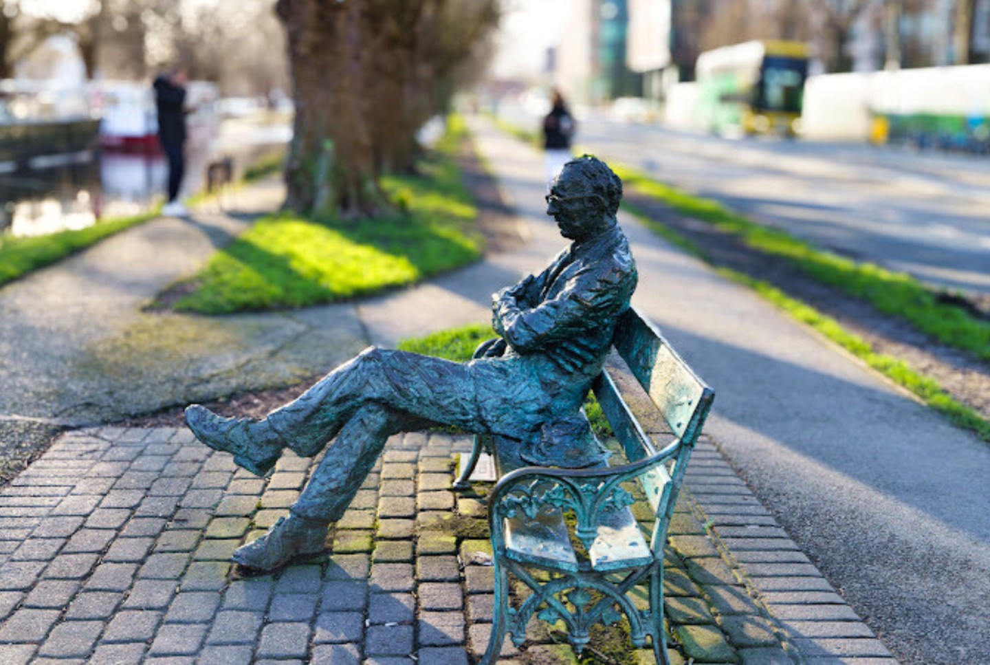 A picture of a statue of a man with his legs crossed on a bench with trees in the background