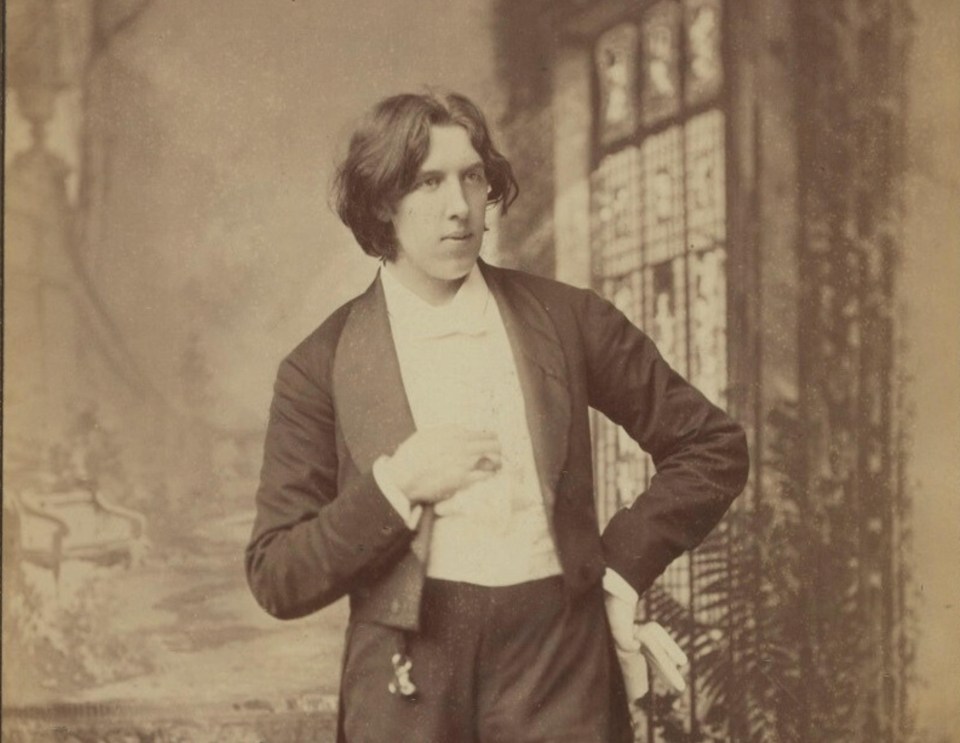 Oscar Wilde stands with a blazer and a white shirt