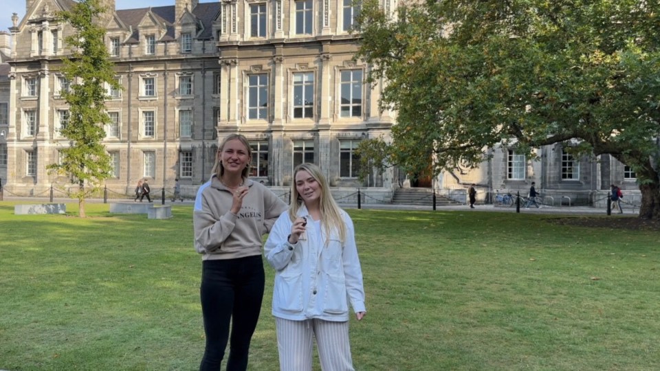 Your two local guides standing in Trinity campus on front of green grass and an old building