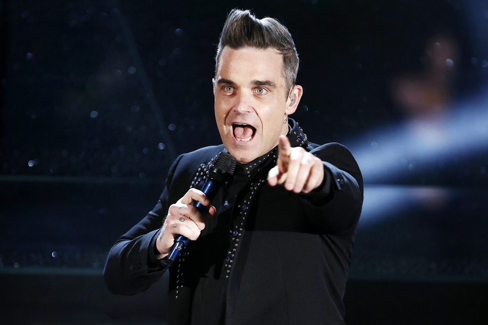 Robbie Williams in black on stage singing into a microphone