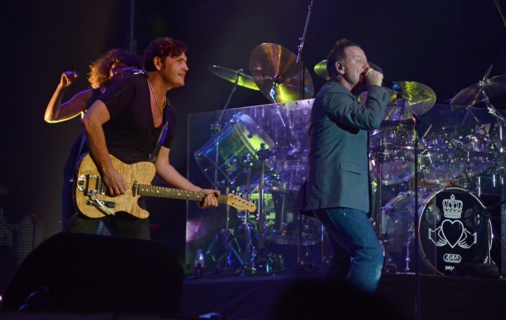 Simple Minds performing on stage with a guitar, drums and microphone