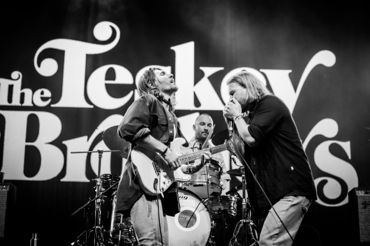 The 3 Teskey Brothers band members on stage with a guitar, drums and microphone