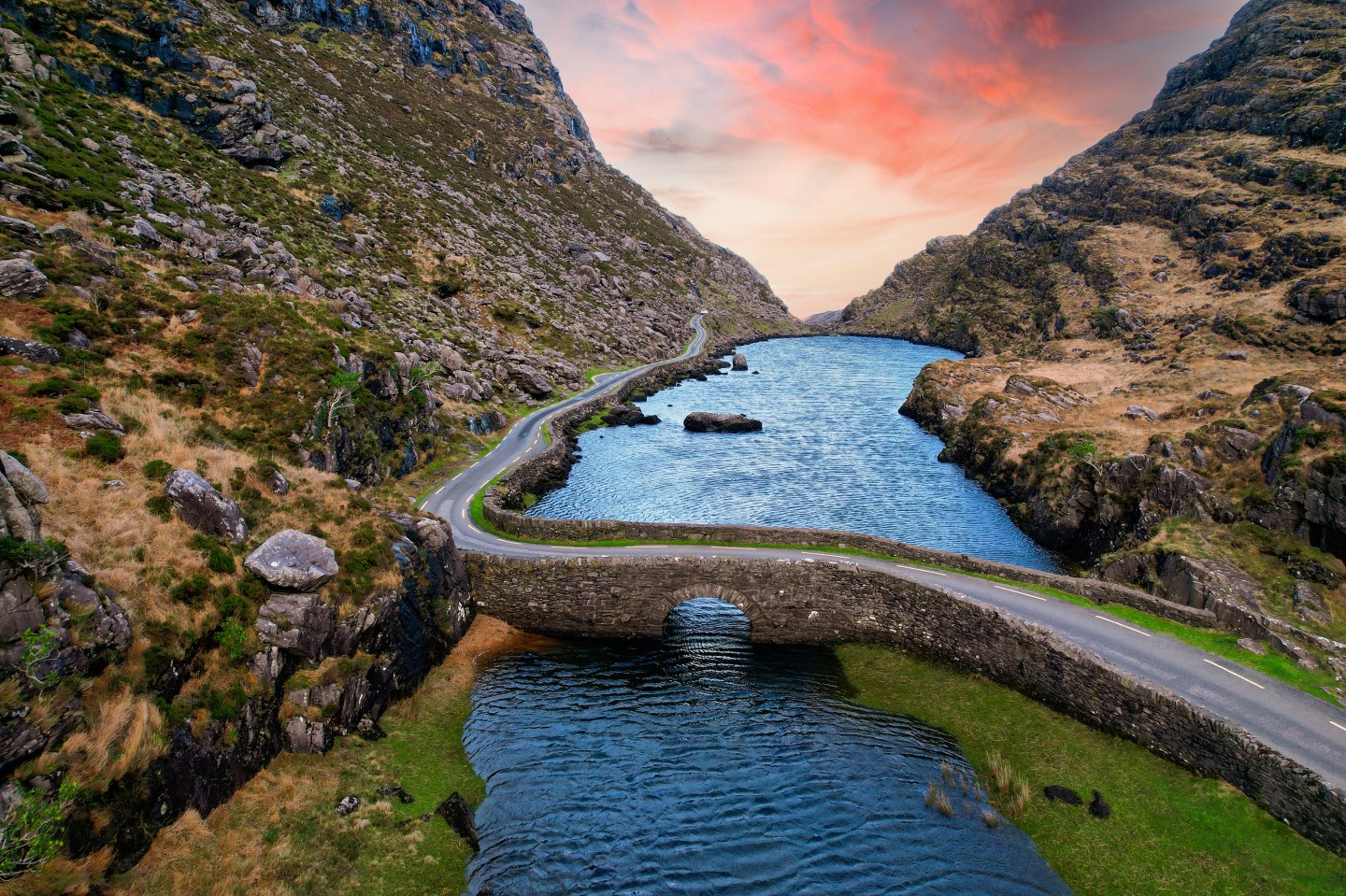 A road runs through a mountainside with a lake underneath