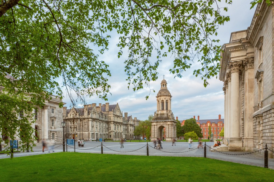 Green leaves of a tree frame the Front Square at Trinity with historic grey buildings in vew